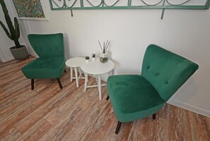 A room with two green armchairs and a small white table, wooden flooring, a potted plant, and a decorative wall piece. - Natale del Grande 21 Stylish Apartment (Roma)
