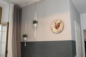 A room with a wall clock featuring a rooster, two hanging macrame planters, and a door on the right. - Natale del Grande 21 Stylish Apartment (Roma)