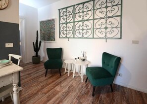 A room with a wooden floor, a green armchair, a white table, and a decorative metal partition. - Natale del Grande 21 Stylish Apartment (Roma)