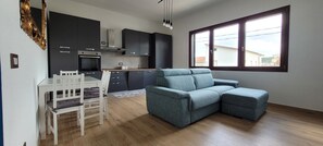 A modern kitchen with dark cabinets, a white dining table, and a blue sofa. - Casa Nue - Deluxe Apartment (Posada)