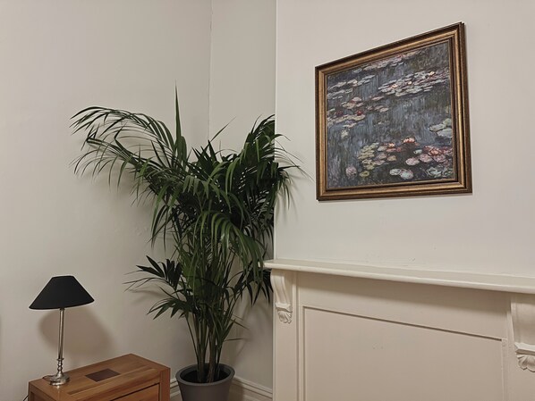 Une pièce avec une plante en pot, un tableau encadré, une lampe et une petite table en bois.