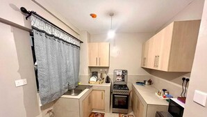 A compact kitchen with a gas stove, oven, and sink. There are wooden cabinets and a small refrigerator. - Martin Aviator Apartement (Kigali)