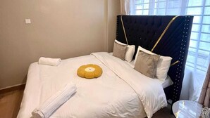 A neatly made bed with white linens, a rolled towel, and a decorative pillow. - Martin Aviator Apartement (Kigali)