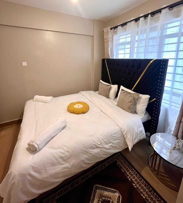 A neatly made bed with white linens, a rolled towel, and a decorative pillow. - Martin Aviator Apartement (Kigali)