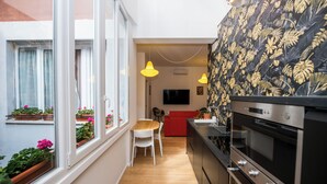 A compact kitchen with a dining area, wooden flooring, and a red sofa.