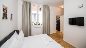 A hotel room with a bed, a TV mounted on the wall, a window with curtains, and a view of the outside.