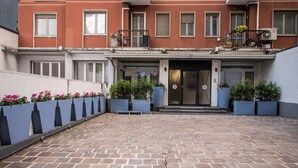A courtyard with a brick floor, potted plants, and a building entrance with a door and steps.