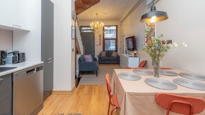A compact kitchen with modern appliances, a dining area with a table set for four, and a living space with a sofa and a chandelier.