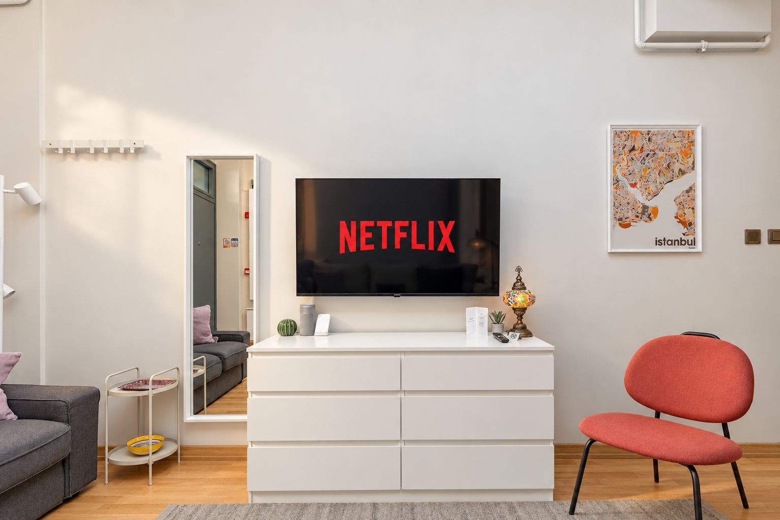 Moderni olohuone, jossa on litteänäyttöinen televisio, jonka ruudulla näkyy teksti »NETFLIX», valkoinen viihdekeskus, punainen tuoli ja seinällä oleva kehystetty Istanbulin kartta.