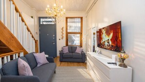 A living room with a staircase, a chandelier, a fireplace, and a television.