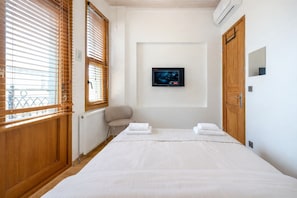 Ein Schlafzimmer mit einem Bett, einem Fernseher, einer Heizung, Holzjalousien und einem Sessel.