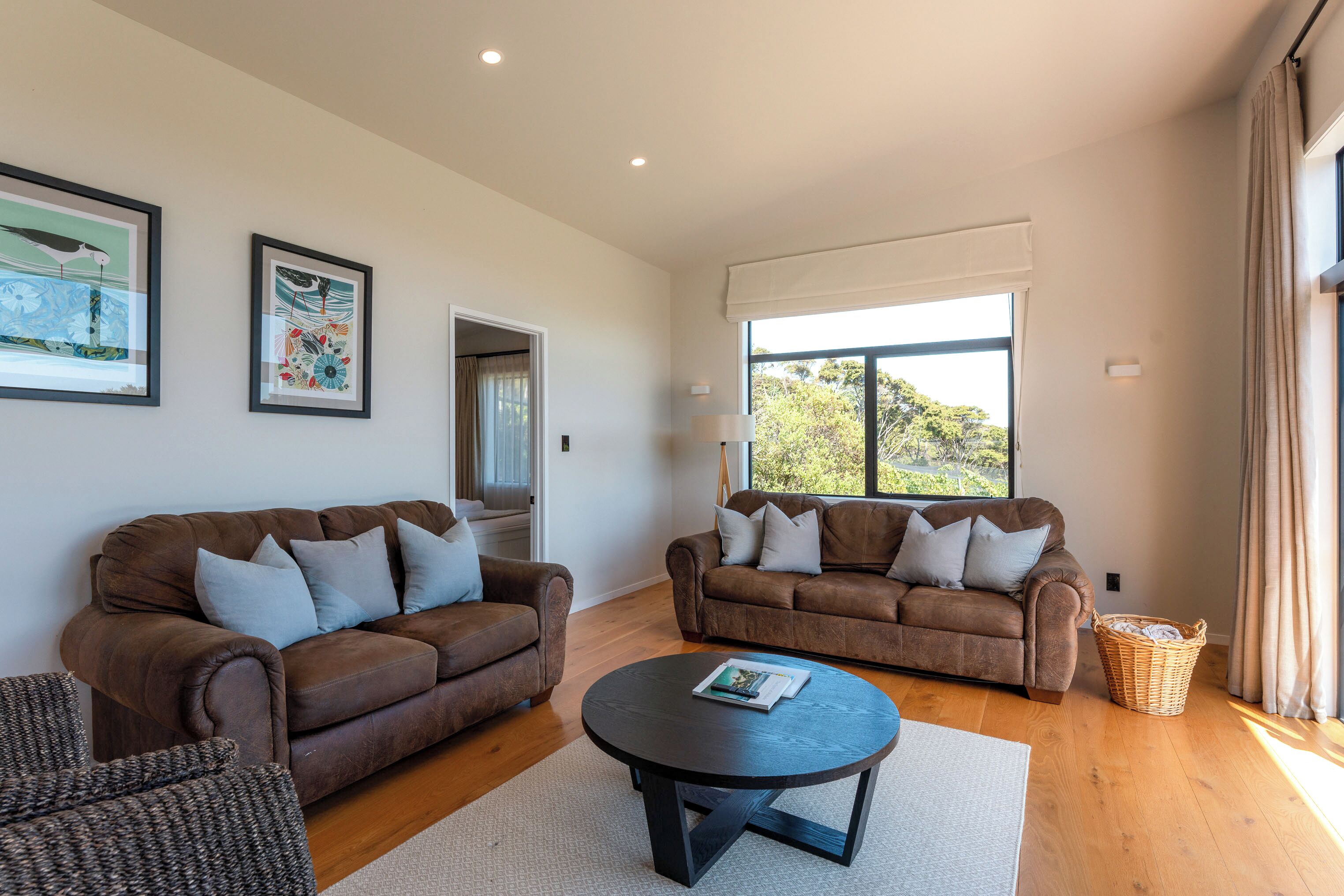 A modern living room with two brown sofas, a round coffee table, and framed artwork on the walls.