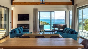 Un salón espacioso con una gran mesa de madera, dos sofás azules, un piano y vistas al mar.