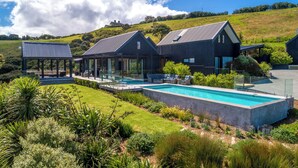 Una casa moderna con piscina, rodeada de exuberante vegetación y una colina al fondo.