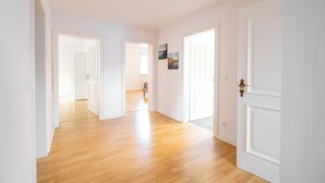 A spacious hallway with wooden flooring and white walls, leading to multiple doors.