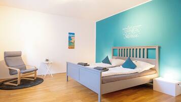 A modern bedroom with a bed, a chair, a small table, and a wall with a decorative sign.