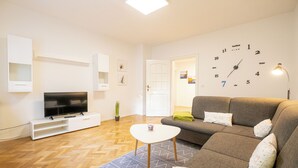 A modern living room with a flat-screen TV, a sofa, a coffee table, and a wall clock.