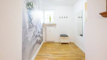 A hallway with a wooden floor, a radiator, a small bench, a window, and a wall-mounted mirror.