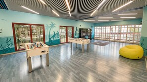 A room with two foosball tables, a yellow bean bag chair, and large windows with a view. - Family coastal escape with water park and beach (Bibione)