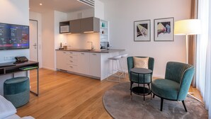 A modern, well-lit living area with a kitchen, a dining table, and two teal chairs.