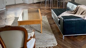 Ein geräumiges Wohnzimmer mit Couchtisch aus Holz, einem dunkelblauen Sofa, einer Kristallleuchter und einem Essbereich mit Tisch und Stühlen.