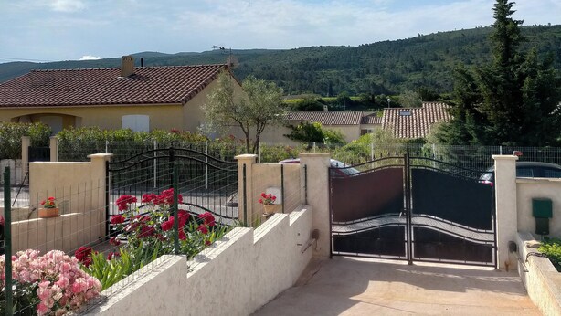 A residential area with a gated entrance, a tiled roof house, and a view of a hilly landscape. - Gite in charming winegrowing village, twenty minutes from Carcassonne. (Comigne)
