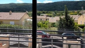 A view from a window overlooking a residential area with houses, a car, and a mountain in the background. - Gite in charming winegrowing village, twenty minutes from Carcassonne. (Comigne)