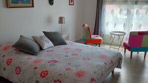 A bedroom with a bed, pillows, a chair, a table, and a window with curtains. - Gite in charming winegrowing village, twenty minutes from Carcassonne. (Comigne)