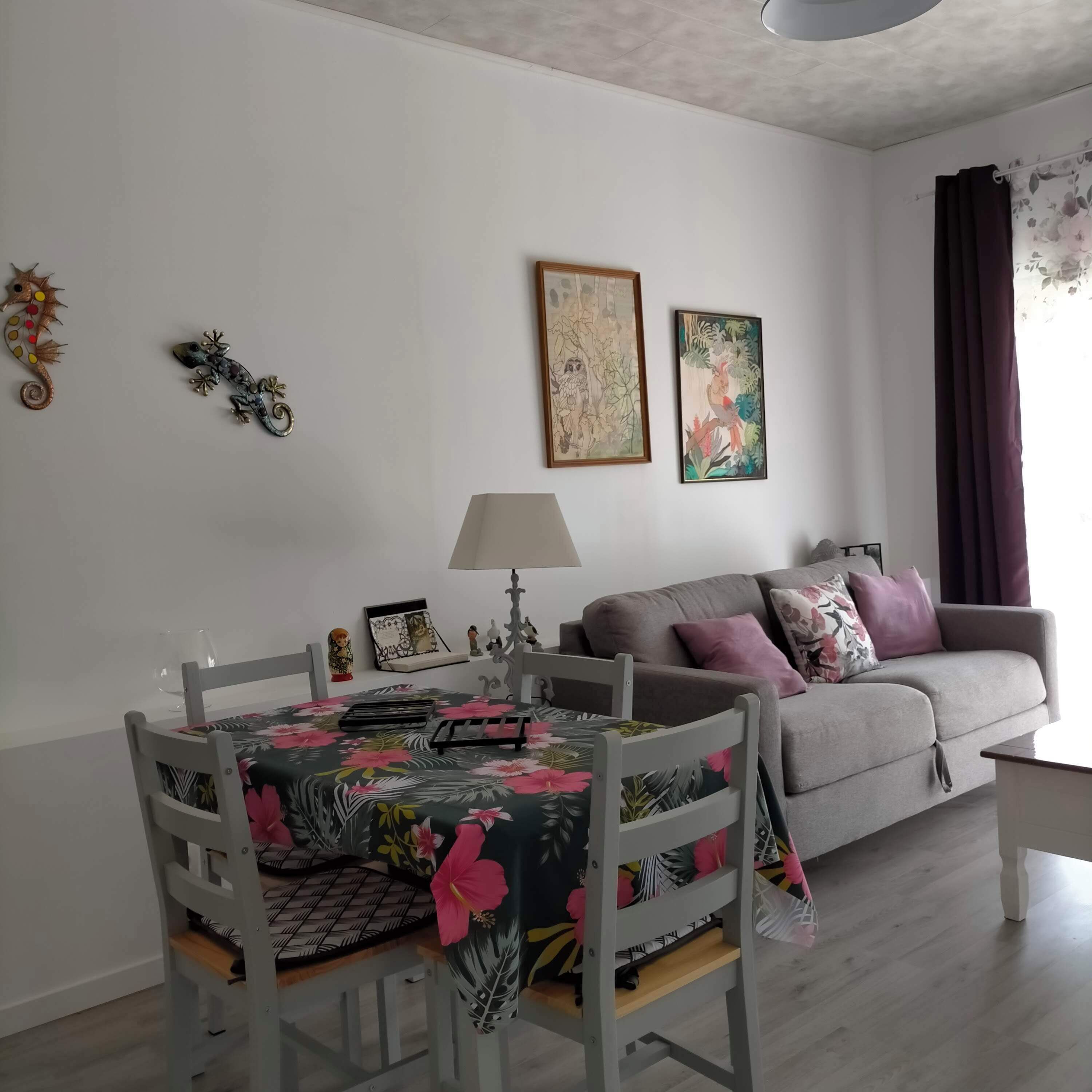 Un soggiorno con un tavolo da pranzo, un divano grigio e due opere d'arte incorniciate appese al muro.