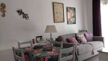 Un soggiorno con un tavolo da pranzo, un divano grigio e due opere d'arte incorniciate appese al muro.