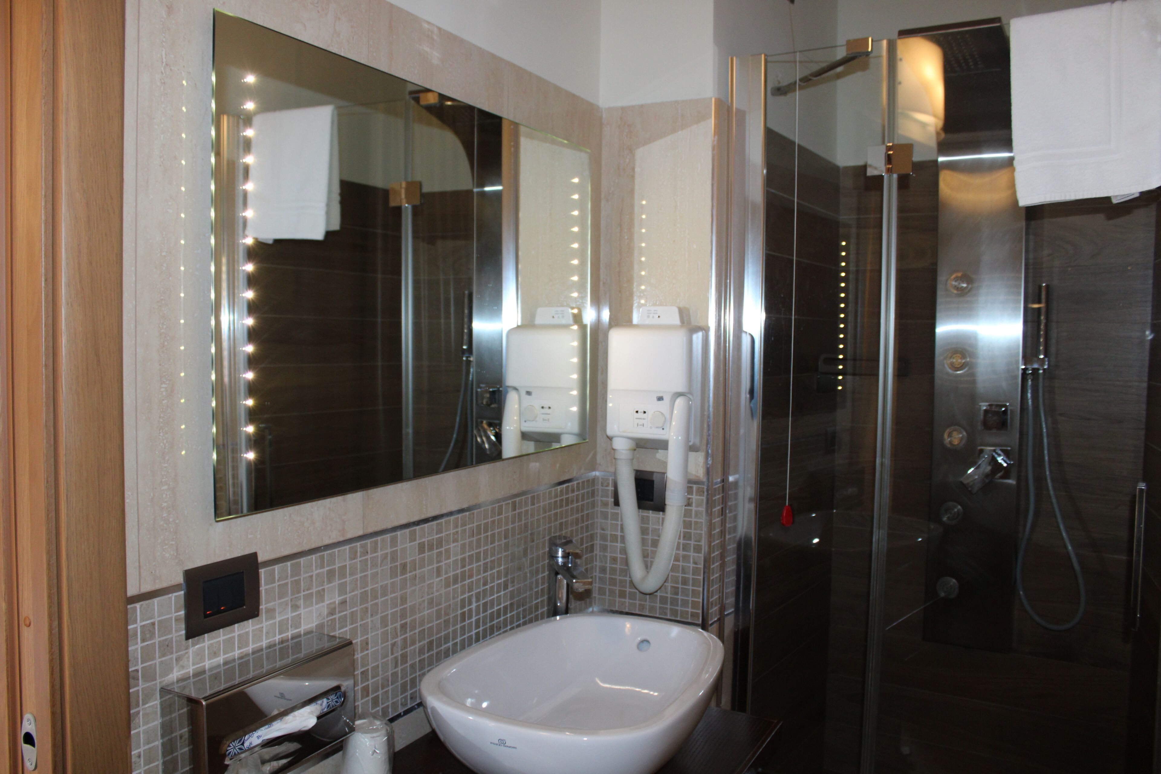A modern bathroom with a large mirror, a sink, a shower, and a towel rack.