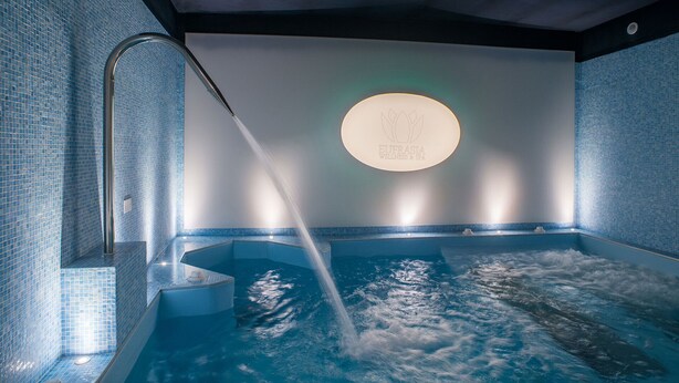 A spa area with a hot tub, a wall-mounted light, and a logo. - Borgo Ospitale (Rotonda)