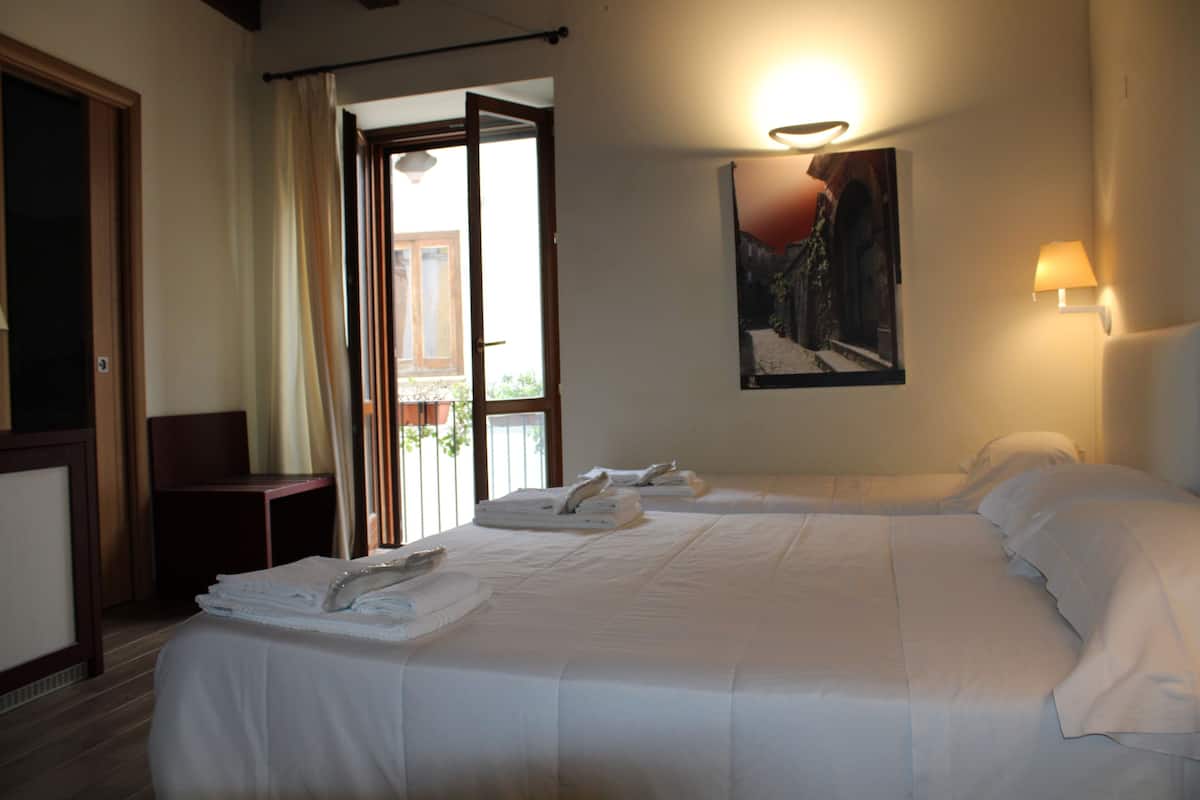 A hotel room with two beds, a balcony, a painting on the wall, and a lamp.