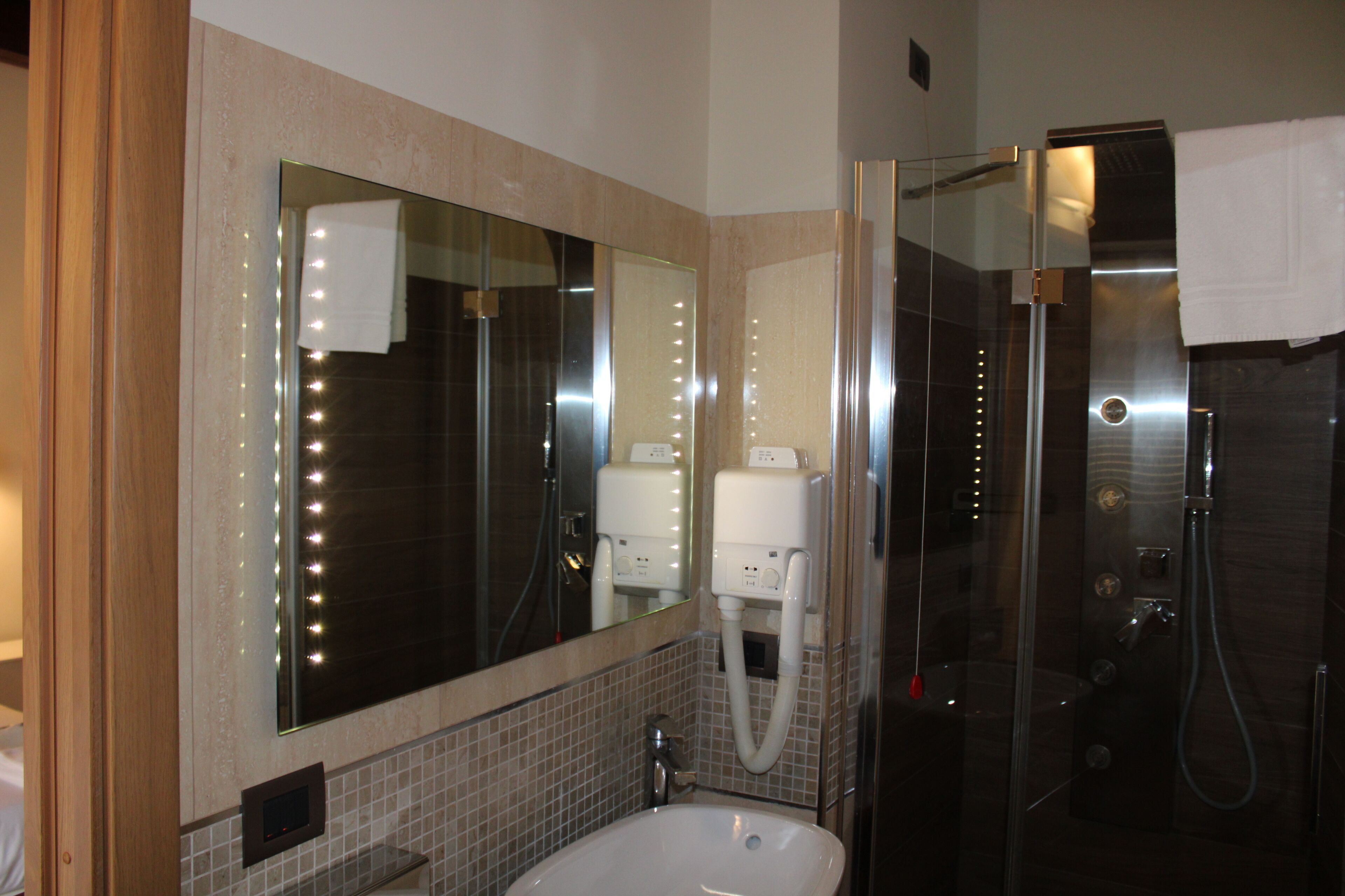 Un baño moderno con un espejo grande, un lavamanos y una ducha con mampara de vidrio.