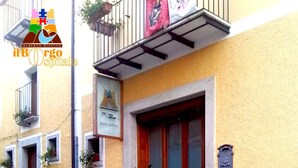 A building with a yellow facade, a red door, and a sign that reads "il BORG ospitale SAN ANNA". There are potted plants and a stone pavement in front. - Borgo Ospitale (Rotonda)