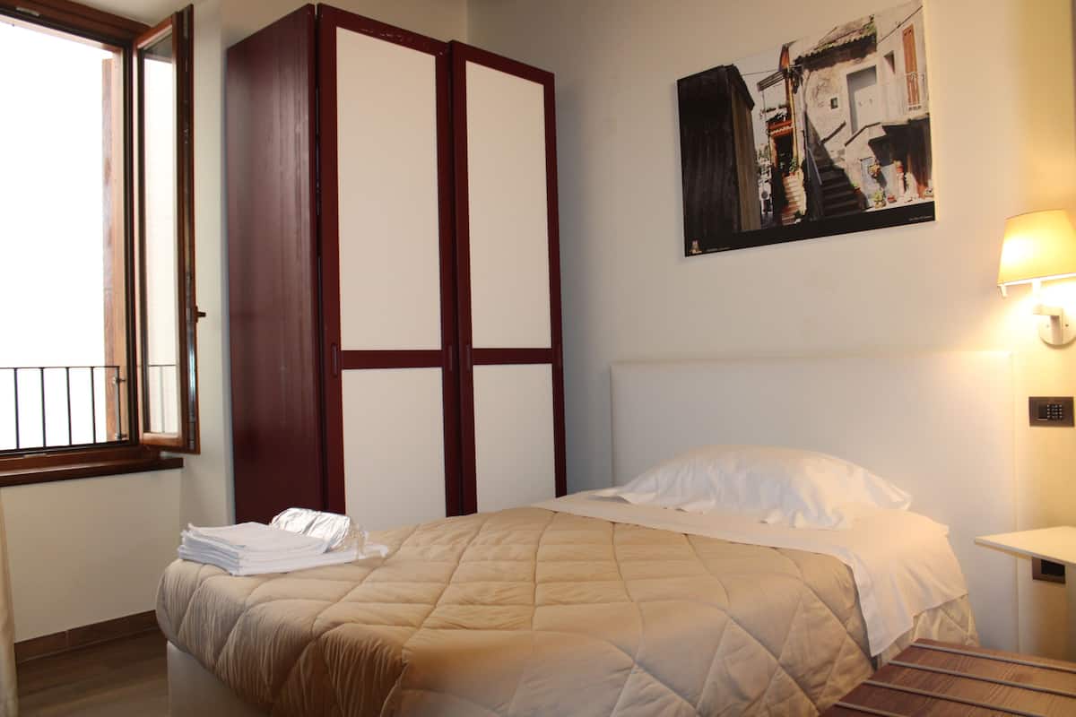A hotel room with a bed, a wardrobe, a painting on the wall, and a window with a view.