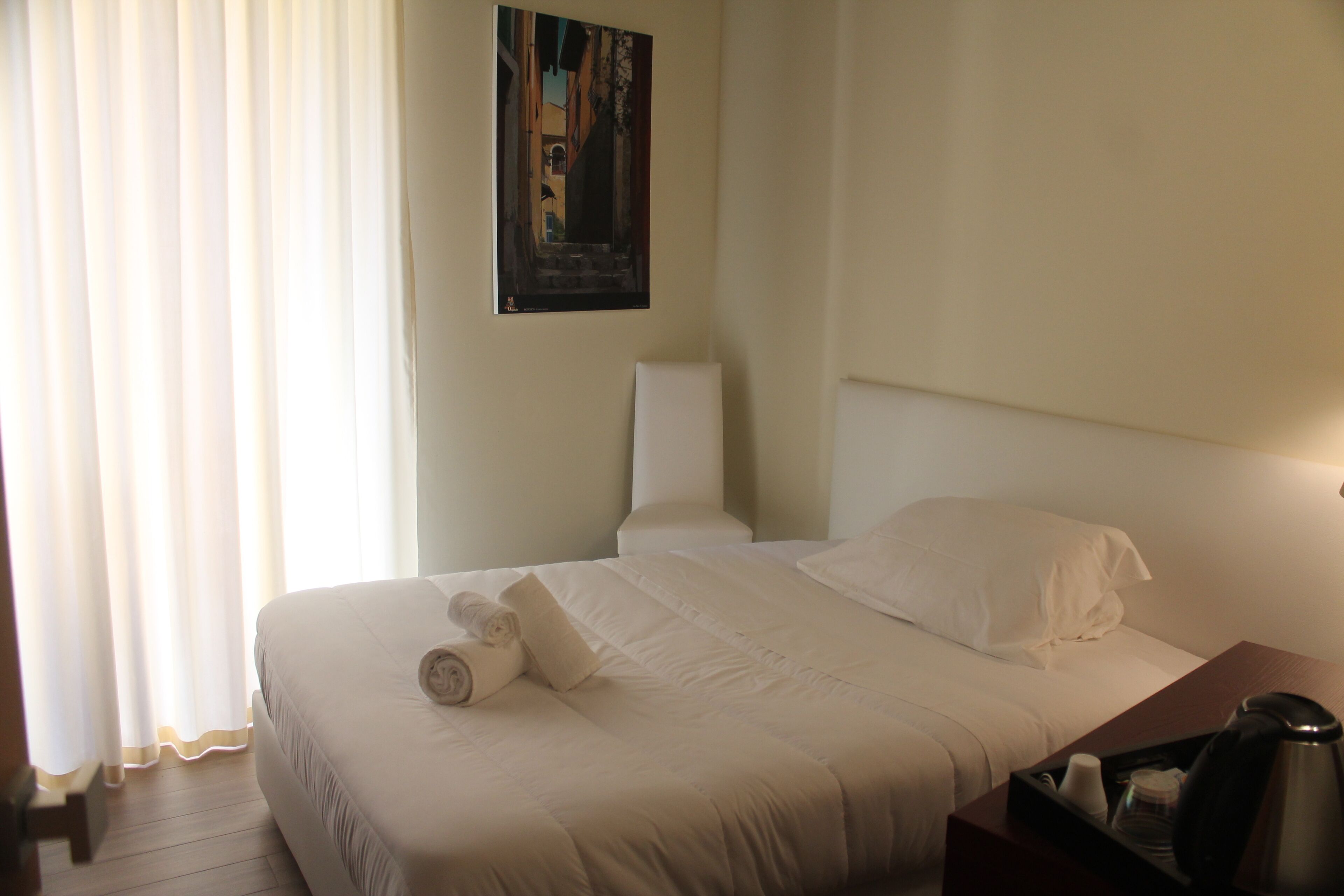 Ein Hotelzimmer mit einem ordentlich bezogenen Bett, einem Bild an der Wand und einem Tablett mit Kaffeekanne und Tassen.