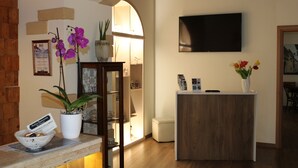 A reception area with a wooden reception desk, a potted orchid, a framed certificate, and a television mounted on the wall. - Borgo Ospitale (Rotonda)