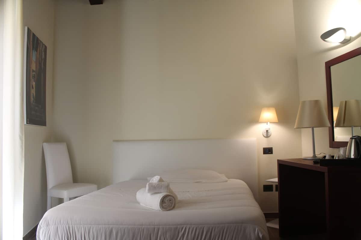 A hotel room with a bed, a chair, a desk, a lamp, and a mirror.