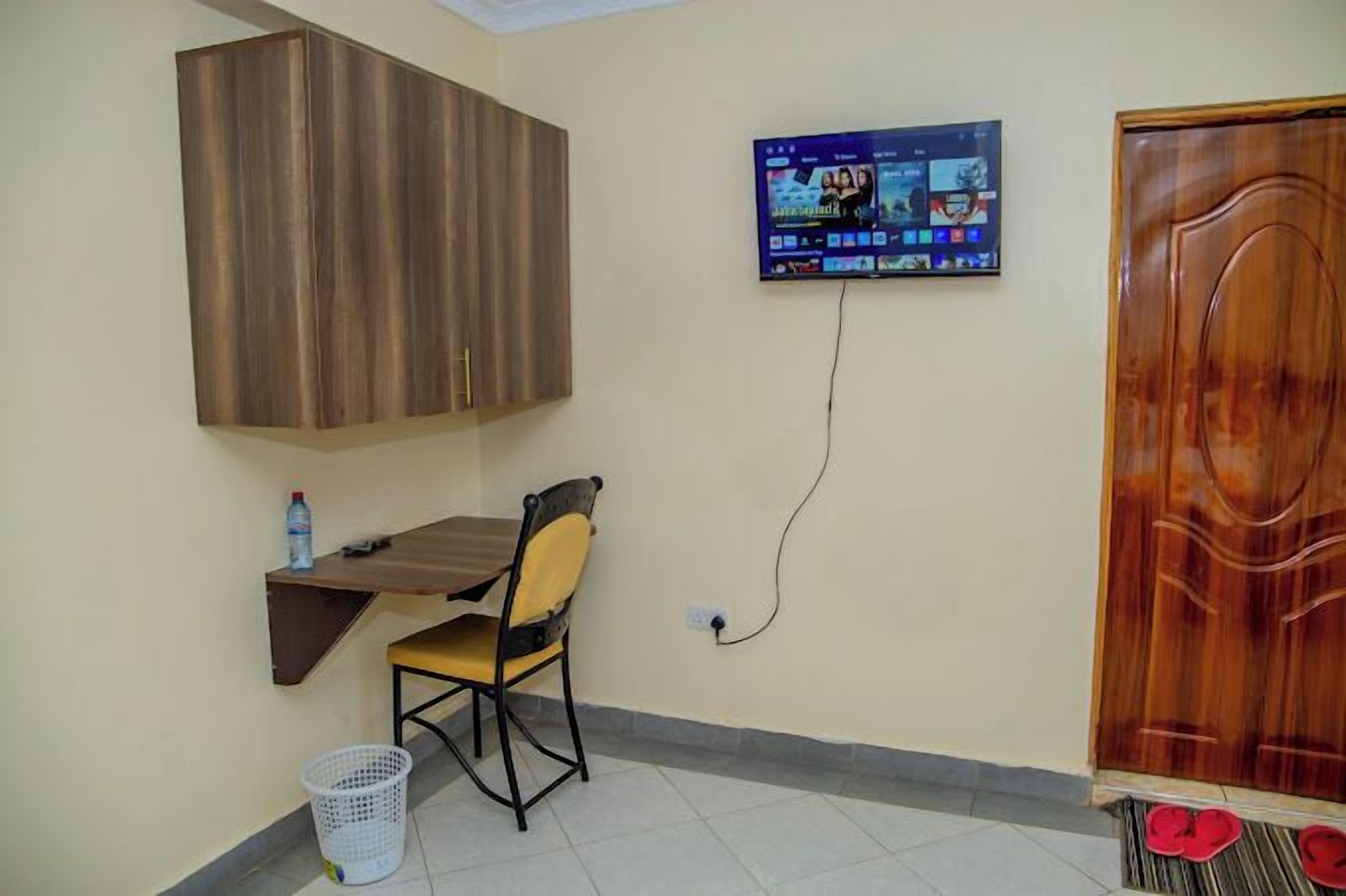 Una habitación con un armario de madera, un televisor montado en la pared, un escritorio con una silla y una puerta.