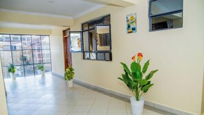 A spacious hallway with tiled flooring, potted plants, and a large window with a view of buildings outside. - Happy Stay Resort Kisii (Kisii)