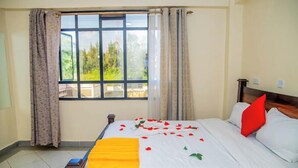 A hotel room with a large window, a bed with white bedding and red pillows, and a yellow throw blanket. - Happy Stay Resort Kisii (Kisii)