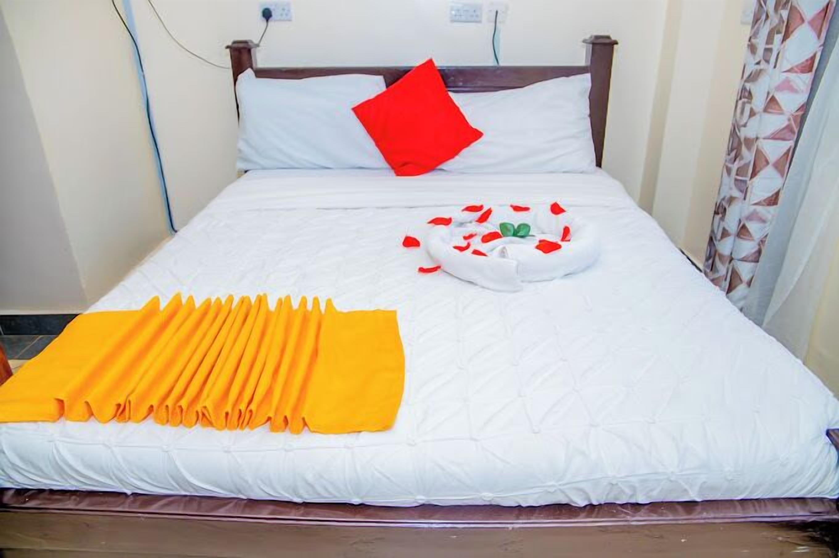 A neatly made bed with white bedding, a red pillow, and a yellow towel arranged on the bed.