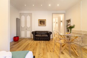 A room with a leather sofa, a glass dining table with chairs, and a red pot. - Crispi 30: A Stylish Apartment (Roma)