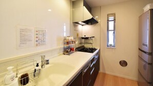 A modern kitchen with a sink, stove, and refrigerator. There is a window providing natural light and a fire safety notice on the wall.