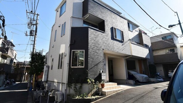 A modern two-story residential building with a flat roof, large windows, and a visible garage.