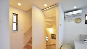 A hotel room with a wooden staircase, a bed, an air conditioning unit, a clock, and a small window.