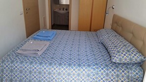 Camera da letto con un letto, un armadio e bagno parzialmente visibile attraverso una porta aperta.