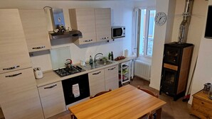 Una cucina funzionale con piano cottura, lavello e forno a microonde. C'è un tavolo da pranzo con sedie e una sveglia appesa al muro.