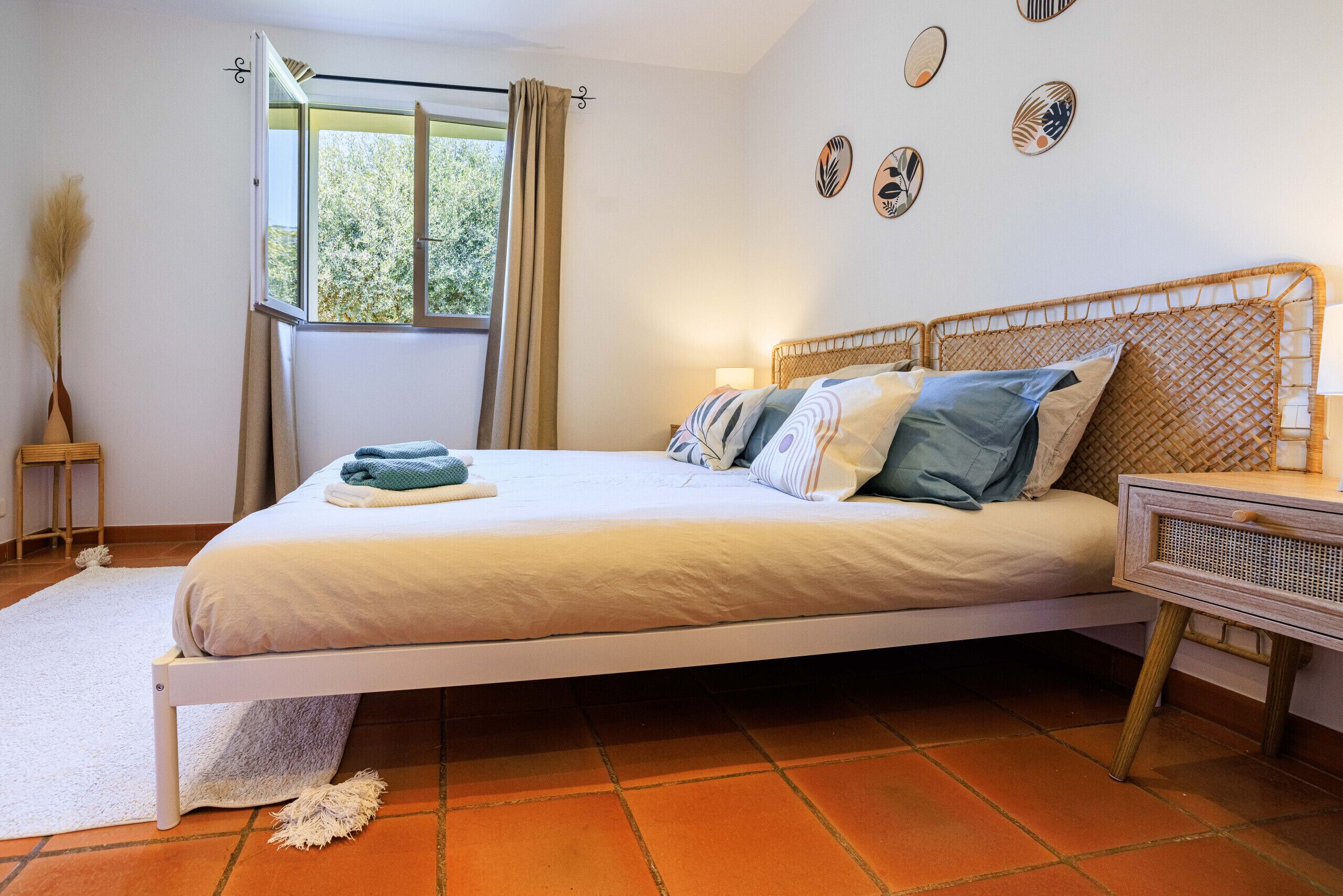 A bedroom with a bed, a bedside table, a window with curtains, and wall decorations.
